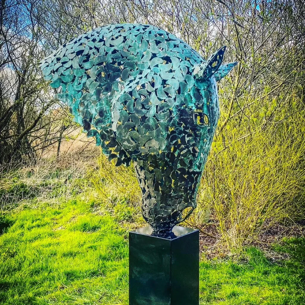 large green horse head sculpture in a wooded area