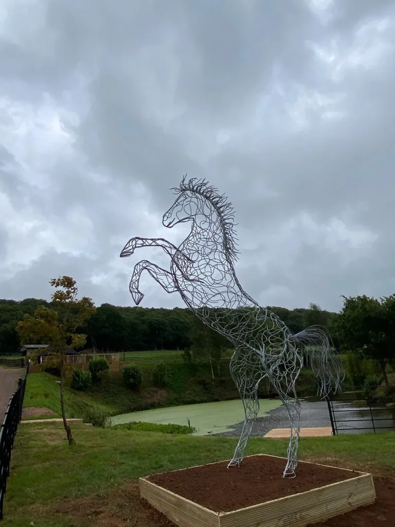 Tall Silver Horse Sculpture In Front Of A Pond