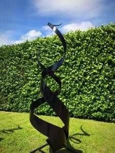 Black Spiral Abstract Sculpture In Front Of Hedge